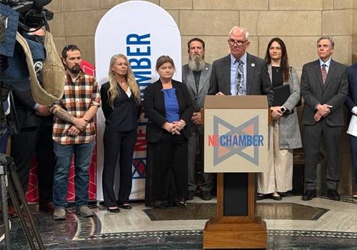 SCC President Dr. Paul Illich speaks at a podium bearing the "NE Chamber" logo at the Nebraska State Capitol for a press conference in front of a TV camera on the left side of the frame. There are approximately eight people standing behind him. The attendees are dressed in business and business-casual attire.