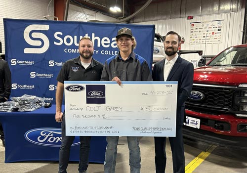 SCC Student Colt Garey stands in front of a Ford truck holding a giant check with a representative from Ford on the right and a technician from TNT on the left