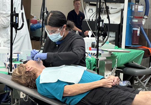Dental assisting student Aliyah Mendoza is wearing face protection while working with a patient reclined in a dental chair at Veterans Mission of Mercy