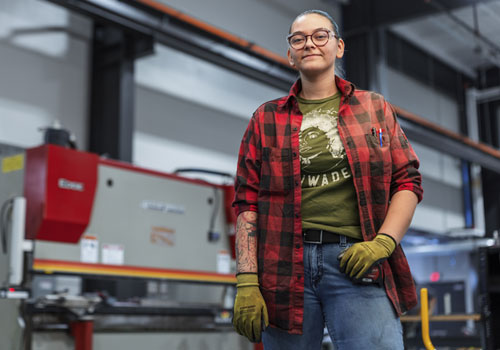 Sapphire Guzman is wearing glasses, a red plaid flannel shirt, and yellow work gloves in SCC’s new Welding Technology Center.