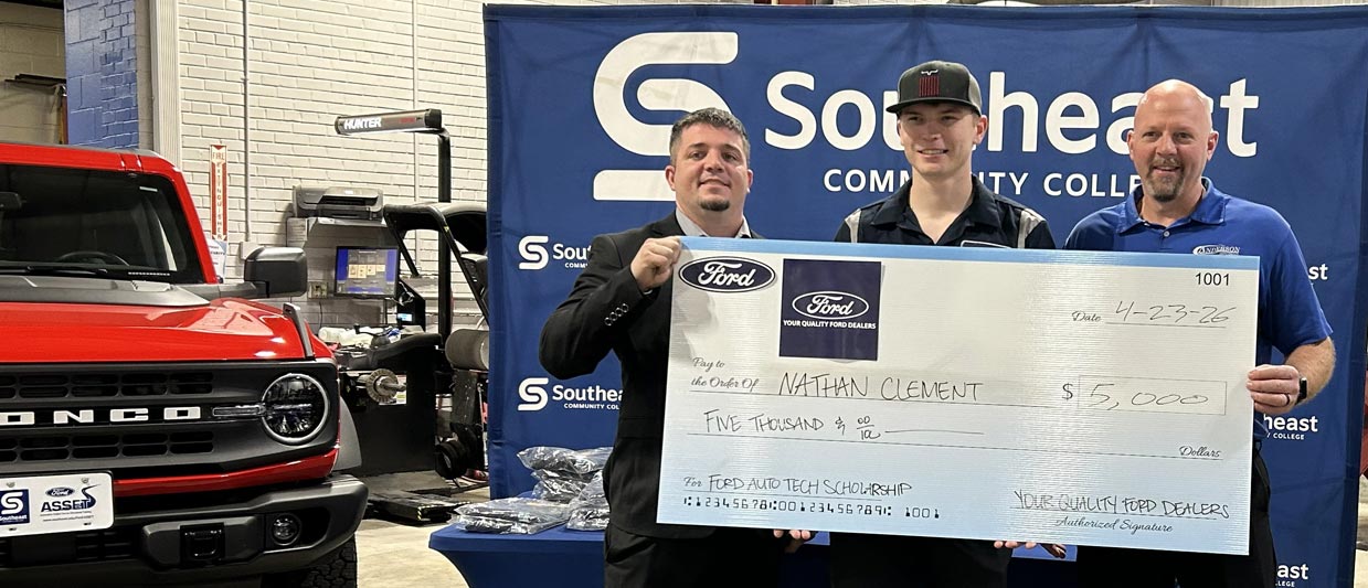 SCC Student Nathan Clement stands in front of a Ford truck holding a giant check with a representative from Ford on the left and a local dealership representative on the right.